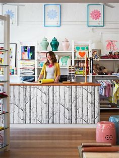 a woman standing at the front desk of a store with lots of items on shelves