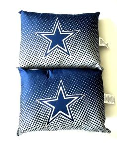 two blue pillows with stars on them sitting next to each other in front of a white wall