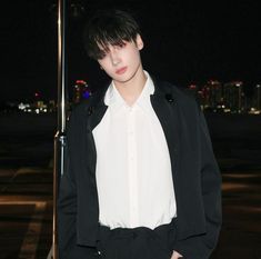 a young man wearing a white shirt and black blazer standing next to a pole