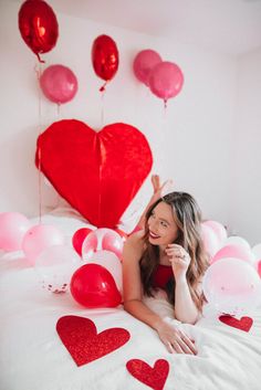 a woman laying on top of a bed surrounded by balloons and heart shaped balloons in the air