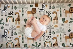 a baby laying on top of a crib next to a wall with giraffes