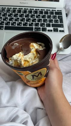 an ice cream sundae is in front of a laptop on a bed with someone's hand