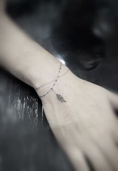 a woman's arm with a tiny arrow tattoo on it and a chain hanging from the wrist