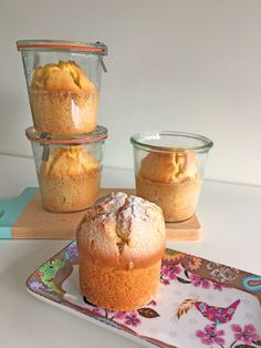 three muffins sitting on a tray next to two glass containers with one muffin in it