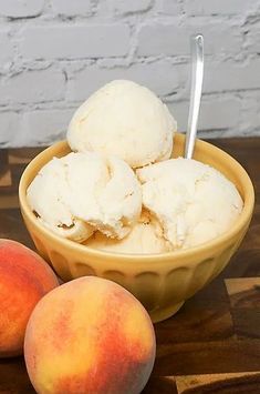 three scoops of ice cream in a bowl next to two peaches on a wooden table