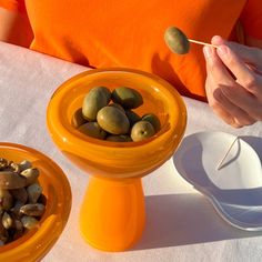 a person is holding a stick over some fruit in bowls on a table with plates