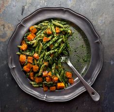 a plate filled with green beans and carrots next to a spoon on a table