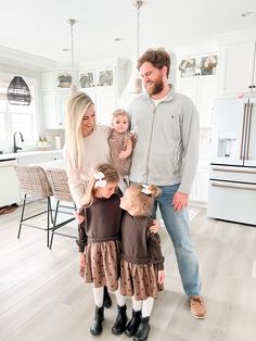 a man, woman and two children are standing in the kitchen with their arms around each other