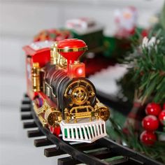 a toy train is sitting on the tracks near christmas trees and presents in front of it