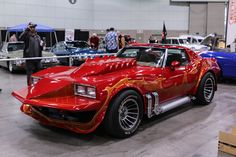 a red car parked inside of a garage next to other cars and people standing around