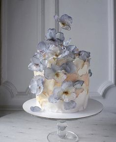 a white cake with blue flowers on it sitting on a glass plate in front of a wall