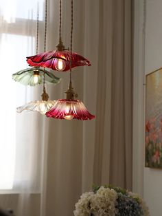 three lights hanging from a ceiling in a room with curtains and flowers on the table