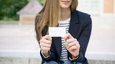 a woman sitting on the ground holding up a business card in front of her face