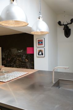 a stainless steel counter top in a kitchen with two lights hanging above it and pictures on the wall