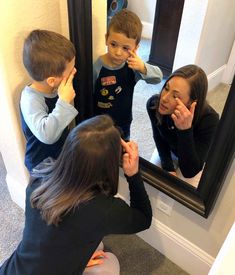 a woman is brushing her teeth in front of a mirror while two children look on