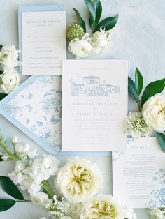 the wedding stationery is laid out with flowers and greenery