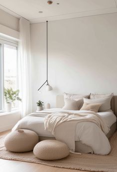 a bedroom with white walls and flooring has a large bed in the center, along with two stools on either side