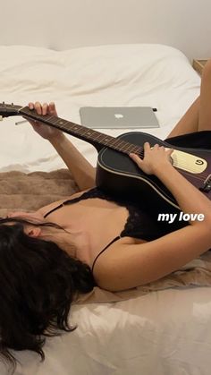 a woman laying on top of a bed holding a guitar