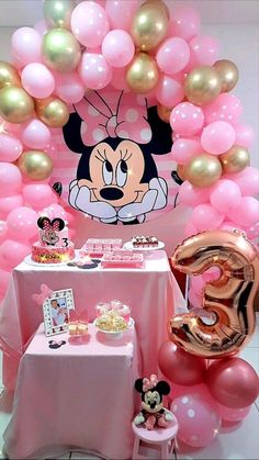 a minnie mouse balloon arch with pink and gold balloons on the table, along with other decorations