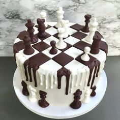 a cake decorated with chess pieces and chocolate icing on a white plate next to a marble wall