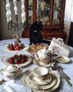 a black cat sitting on top of a table next to plates and bowls filled with food