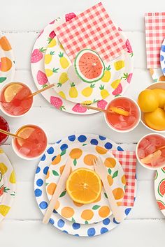 colorful plates with fruit and utensils laid out on a white wooden table top