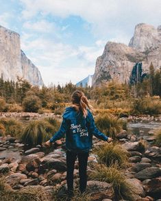 a woman standing on rocks in the middle of a river with mountains in the background