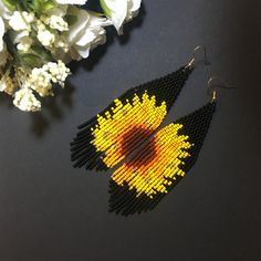 a pair of yellow and black seed beaded earrings next to white flowers on a table