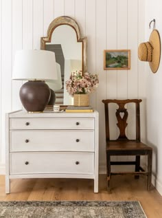 a white dresser sitting next to a wooden chair and lamp on top of a table