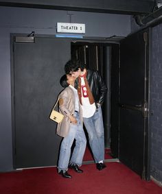 two people are kissing in an elevator with red carpet and black walls, while the man is wearing a brown jacket