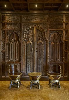 two wooden chairs sitting in front of an ornate paneled wall with carvings on it