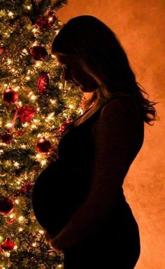 a pregnant woman standing in front of a christmas tree