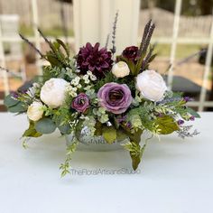 a vase filled with flowers sitting on top of a white table covered in greenery