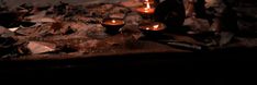 two lit candles sitting on the ground in front of some rocks and leaves at night