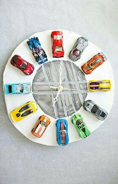 a clock made out of toy cars sitting on top of a white table with grey background