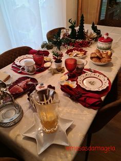 a table set for christmas dinner with plates, cups and saucers on the table