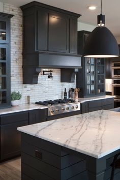 a large kitchen with black cabinets and marble counter tops, along with stainless steel appliances