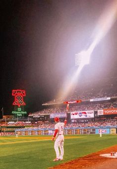 a baseball player holding his bat up in the air on a field at night time