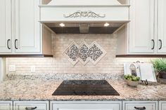 a kitchen with white cabinets and marble counter tops, an oven hood over the stove