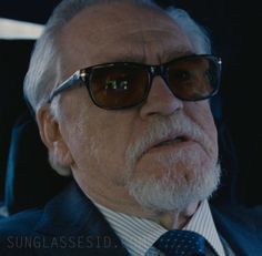 an older man wearing sunglasses and a suit sitting in the back seat of a car