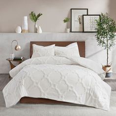 a bed with white comforter and pillows in a room next to a potted plant