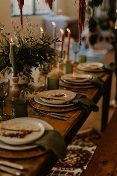 the table is set with plates and silverware, candles, and greenery in vases