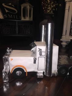 a toy truck made out of tinfoil on top of a wooden floor in front of a fireplace