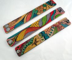 three different colored wooden knives on a white surface