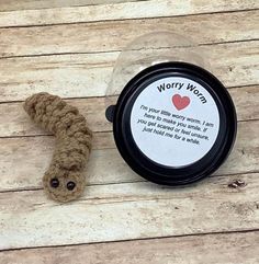 a small crocheted worm sitting next to a container with a message on it