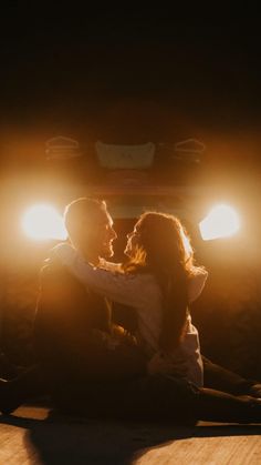 a man and woman sitting on the ground in front of a truck with their arms around each other