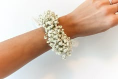 a woman's arm wearing a bracelet with white flowers on it and a ring