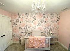 a baby's room decorated in pink and gray with floral wallpaper, chandelier and crib