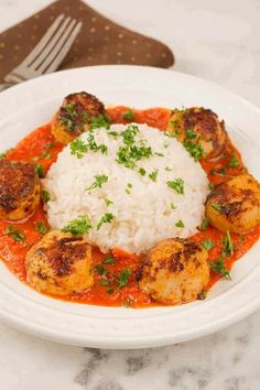 a white plate topped with meat and rice on top of a table next to a fork