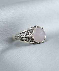 Elevate your style with this stunning Handmade Filigree Art Rose Quartz Gemstone Women Silver Cocktail Statement Ring. The 10mm cabochon round-cut Rose Quartz gemstone set in an elegant silver band measures 13.50mm in length and width, creating a beautiful contrast between the soft pink hues of the gemstone and the silver metal. Crafted with intricate details that showcase the beauty of filigree, an ancient art form originating from Mesopotamia and Anatolia, this exquisite ring is a true work of Rose Gold Sterling Silver Crystal Ring, Sterling Silver Rose Gold Crystal Ring, Elegant Silver Rings With Rose Design, Round Rose Quartz Promise Ring, Elegant Pink Cabochon Rings, Rose Classic Formal Jewelry, Classic Rose-colored Formal Jewelry, Classic Pink Cabochon Rings, Rose Quartz Crystal Promise Ring